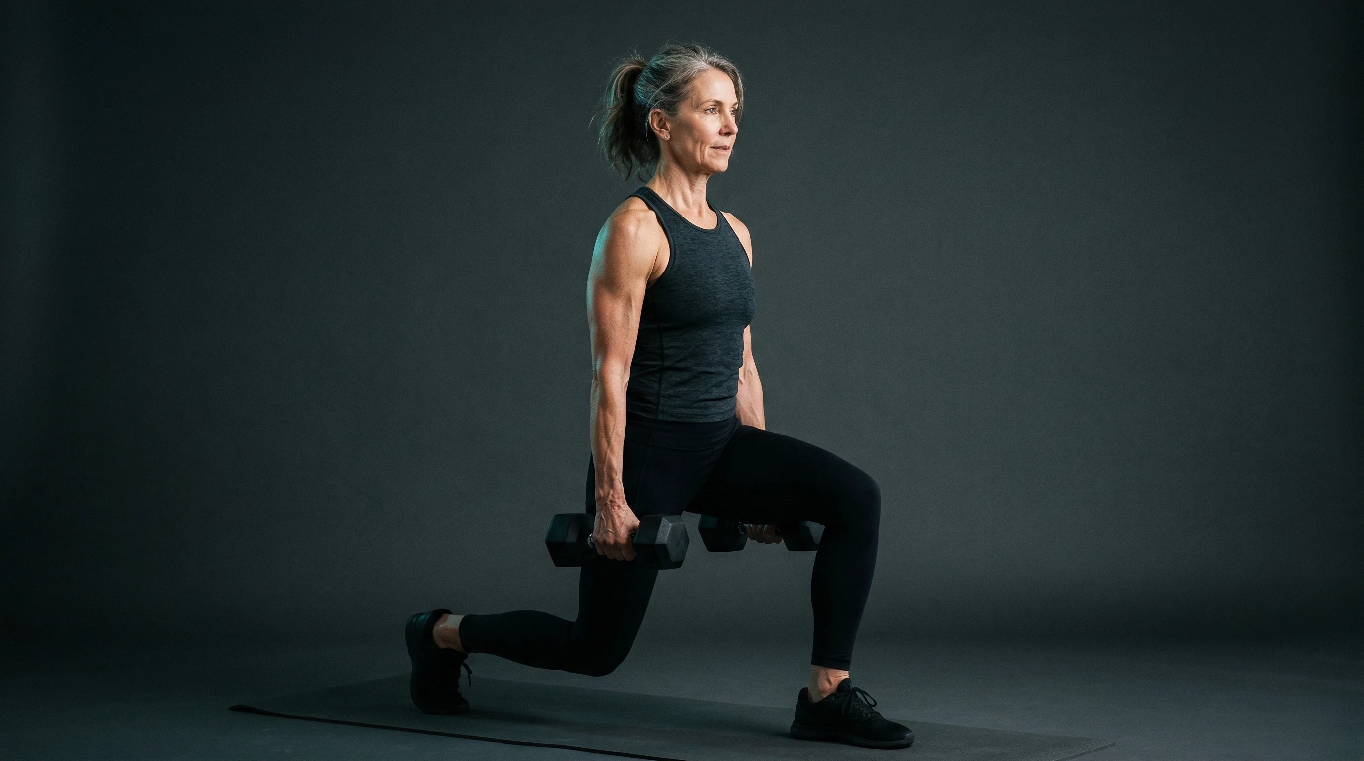 Frau ab 50, athletisch, beim Krafttraining mit Kurzhanteln, dunkler Hintergrund mit Teal-Akzent